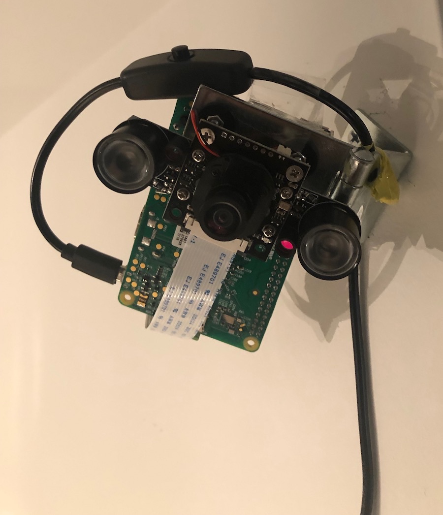 A compact Raspberry Pi with a camera module and two lenses, mounted flat against a ceiling