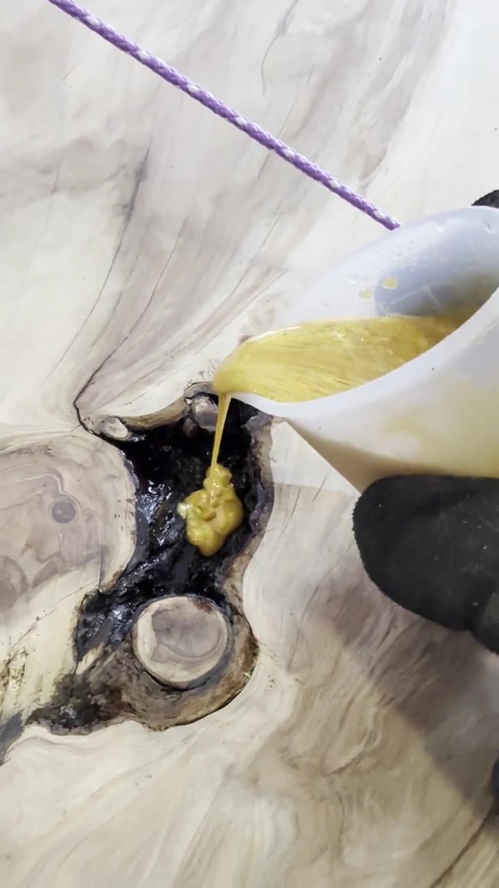 Pouring gold epoxy from a cup into a dark knot hole in the slab