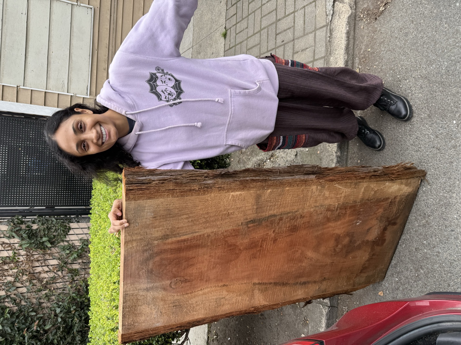 Roshni standing next to the raw redwood slab on the sidewalk after pickup