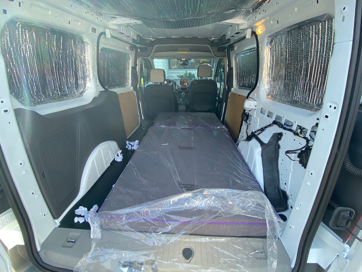 Two mattresses still in plastic, laid end to end along the insulated floor of the van