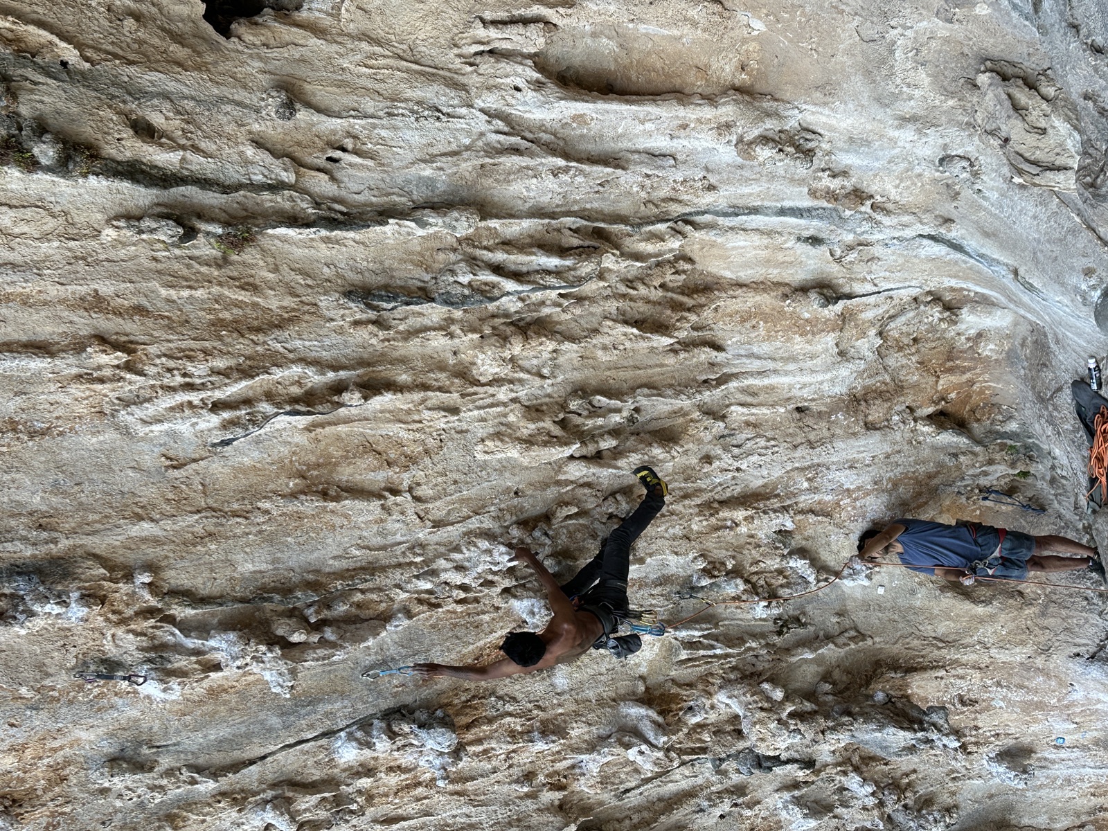 Reaching for the second bolt on DNA, belayer on the ledge below