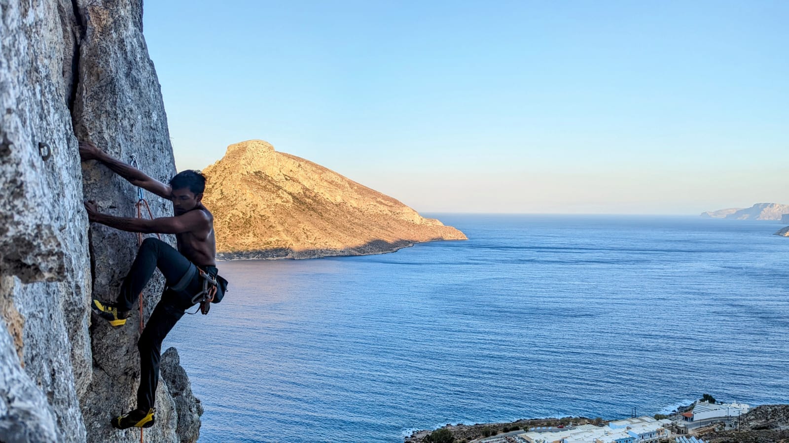 Climbing a grey limestone face with Telendos and the village below in late light